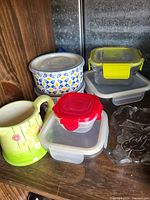 Photo showing all items including ceramic mug, several food storage containers with colored lids, and a decorative clear glass leaf-shaped dish.