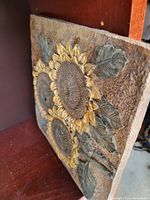 Square stone decor with sunflower design showing textured petals, leaves, and flower centers.