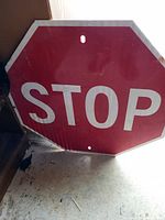 Front view of octagonal metal stop sign with red background and white STOP lettering. Shows wear and mounting holes.