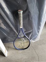 Full view of a blue tennis racket with a white worn grip against a gray background