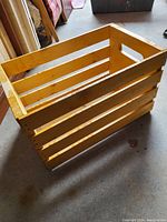 Angled side view of wooden box showing slatted sides and one cutout handle