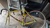 Yellow Aero vintage road bike in heavily used condition, missing front tire and with rear tire needing replacement.