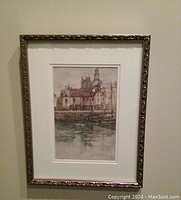 Framed watercolor artwork showing detailed buildings by water with boats and reflections.