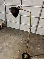 Floor lamp with bronze finish and adjustable arm, black shade, round base shown in a garage setting.