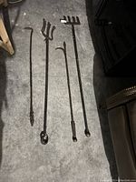 Set of four cast iron fireplace tools laid out on a concrete floor, showing twisted handles and tool ends for managing firewood and ashes.