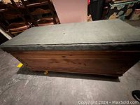 Full view of the wooden cedar chest with green cushioned top seat visible.
