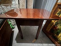 Wooden drop leaf table with leaf extended showing polished surface and four legs.