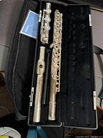 Opened fabric-lined case showing disassembled silver flute sections and Yamaha booklet