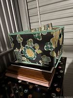 Floral-patterned fabric bin placed on top of a stack of frames showing the bin and the stacked frames underneath it.