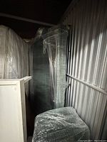 Side view of green couch wrapped in plastic, showing upholstery texture and shape.