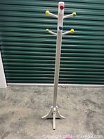 Photo of free-standing kids coat rack with eight multicolored peg hooks against a green shutter and concrete floor background.