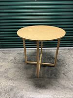 Front view of the large round wooden table showing its round top and four legs connected by cross braces.