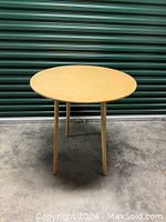 Side view of medium round wooden table showing three cylindrical legs and smooth tabletop.