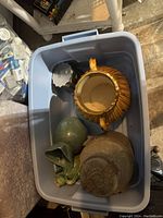 Overhead photo of four assorted vases inside a blue plastic bin, showing different shapes, colors, and conditions.