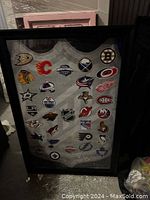 Photo showing the large framed collage of various NHL team logos on a white background with black frame and glass coverage.