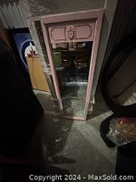 Full-length pink framed rectangular girls' mirror with carved floral detail at the top panel placed vertically against wall in dim lighting.