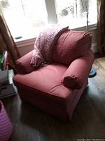 Red upholstered armchair positioned near a window with a matching red textured throw blanket draped over the backrest, displayed on wood flooring.