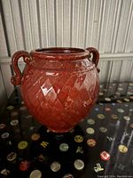 Front and angled view of the red ceramic vase with diamond pattern and two curled handles, glossy finish visible.