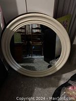 Front view of large round mirror with white frame, reflective surface visible