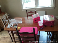 Photo of wood dining table with some items placed on top, showing surface and part of chairs.