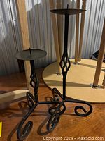 Two black wrought iron candle holders, one smaller and one larger, standing side by side showing their height difference and design details.