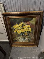Front view of framed oil painting showing yellow flowers in clear vase on table with lace doily.