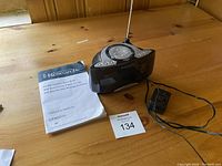 Photo showing Emerson Research All-Alert Clock Radio CKW2000 with remote and owner's manual placed on wooden surface.