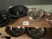 Shelf with black bundt pans, silver fluted cake pan, small copper molds, and silver mixing bowls below.