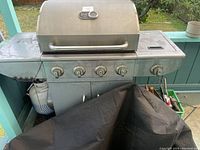 Side view of Broil Chef four-burner gas barbecue grill with propane tank storage below and a black grill cover partially placed.