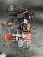 Photo showing all assorted barbecue utensils including skewers, spatula, tongs, grill baskets, fork, and packaged items.