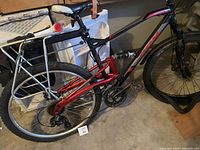 Photo showing side view of the red and black mountain bike with rear suspension and metal rear rack. Rear tire and frame clearly visible.