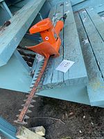 Full angled view of the Orange Black & Decker hedge trimmer resting on weathered blue wood boards. Shows blades and orange body with black trigger handle.