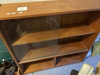 Front view of wooden shelving unit with glass sliding panel covering middle shelves.