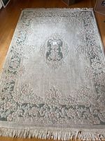 Full view of rectangular area rug on hardwood floor showing floral border and center medallion with fringe