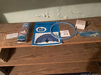 Photo showing the embroidery kit contents on a wooden bench: two blue embroidery hoops, an instruction booklet 'Friends to Framed' with duck design, a brochure for Easy Patch Automatic Embroidery Machine, calendar clipping and seller tag.