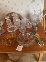 Table with assortment of glass cutware and amber glass serving dishes, metal box and utensils with wooden handles