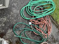 Three coiled garden hoses, two green and one brown, laid on driveway or patio next to grass.