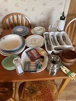 Table with plates, flatware, kitchen utensils, wooden bowls, glass salt shaker and siphon bottle arranged.