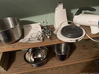 Full view of Sunbeam Mixmaster stand mixer base, metal beaters and mixing bowls on wooden shelf