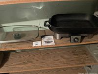 Black electric griddle with adjustable dial and rectangular glass lid on wooden surface