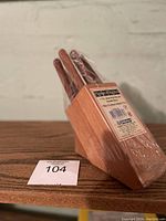 Seven steak knives with wooden handles in a wooden block, still wrapped in plastic packaging with label visible.