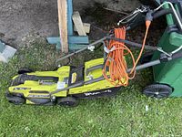 Side view of electric lawn mower with orange power cord wrapped on handle and grass catcher attached.