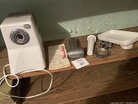 Electric meat grinder with all disassembled parts laid out on a wooden surface, showing the main motor housing, metallic feed tube, screw auger, blade, grinding plate, plastic food pusher, feeding tray, and a Moulinex cloth bag.