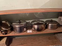 Four stainless steel pots displayed on a shelf showing variety of sizes and lid styles.