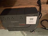 Black APC Back-UPS ES 550VA UPS with power cable and seven power outlets visible on top; device laid on wooden floor.