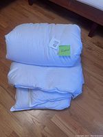 Photo of folded and rolled white queen size duvet placed on wooden floor with visible wooden bed frame.