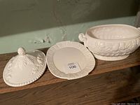 Photograph showing detached lid and smaller oval tray, highlighting detailed embossed design on white ceramic