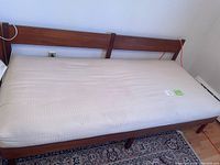 Single wooden bed frame with headboard and beige mattress in a room, showing full bed side and mattress surface.