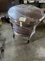 Front and top view of small wooden entry table wrapped in plastic wrap, showing the scalloped top and drawer.