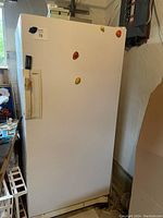 Front view of white stand up freezer with a few magnets on the door and key taped to handle.